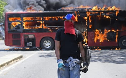 An opposition demonstrator walks near a bus in flames during clashes with soldiers loyal to Maduro - Credit: AFP