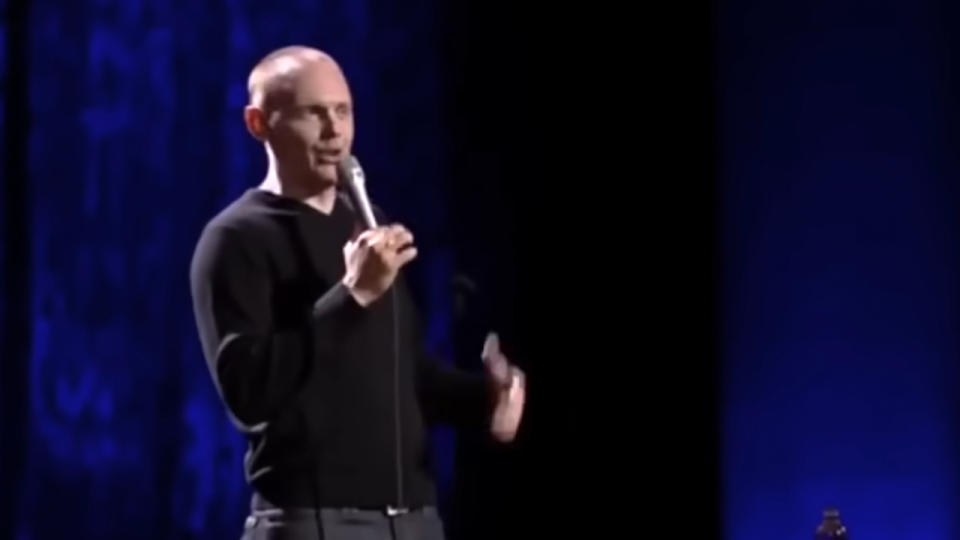 Bill Burr making a joke on stage, wearing a black shirt