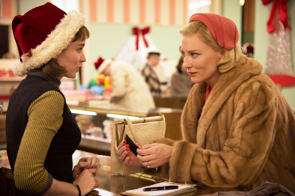 Rooney Mara and Cate Blanchett in a shopping scene from "Carol," discussing over a purse on a counter. Rooney wears a Santa hat; Cate is in a fur coat