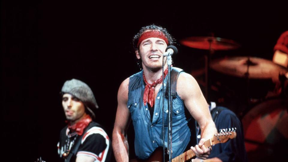 bruce springsteen standing behind a stage microphone and playing the guitar during a concert