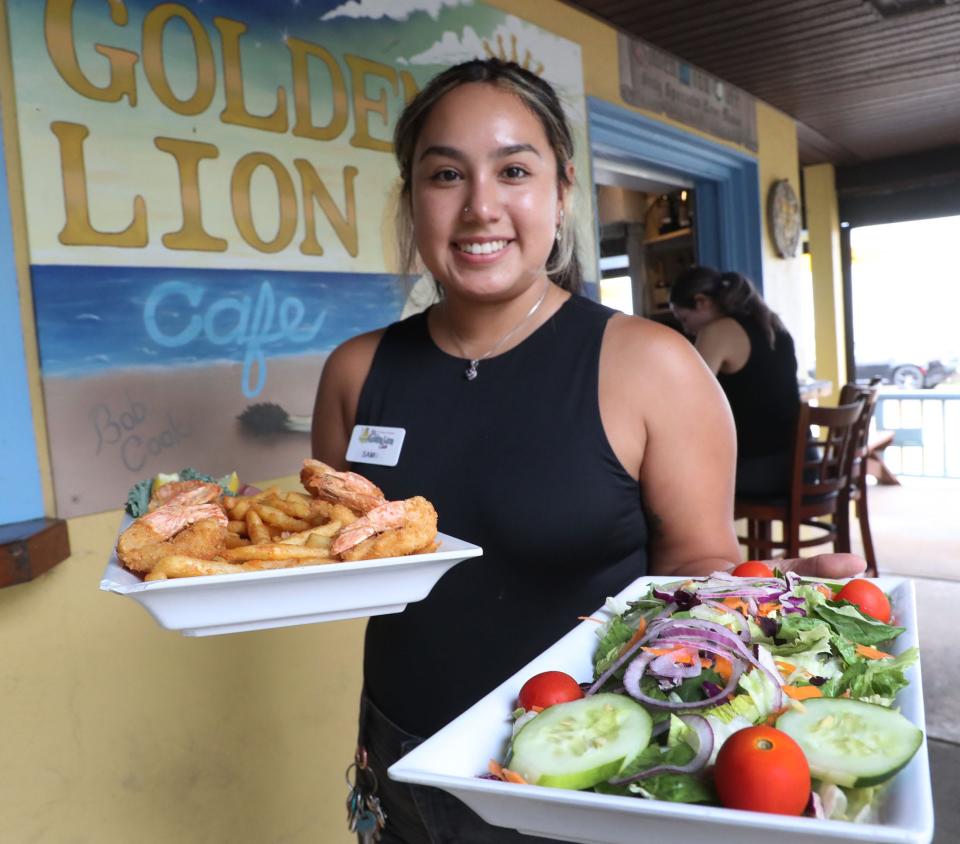 Server Sam Garcia heads to a table with an order of fried shrimp, French fries and a large salad at the Golden Lion Cafe in Flagler Beach.