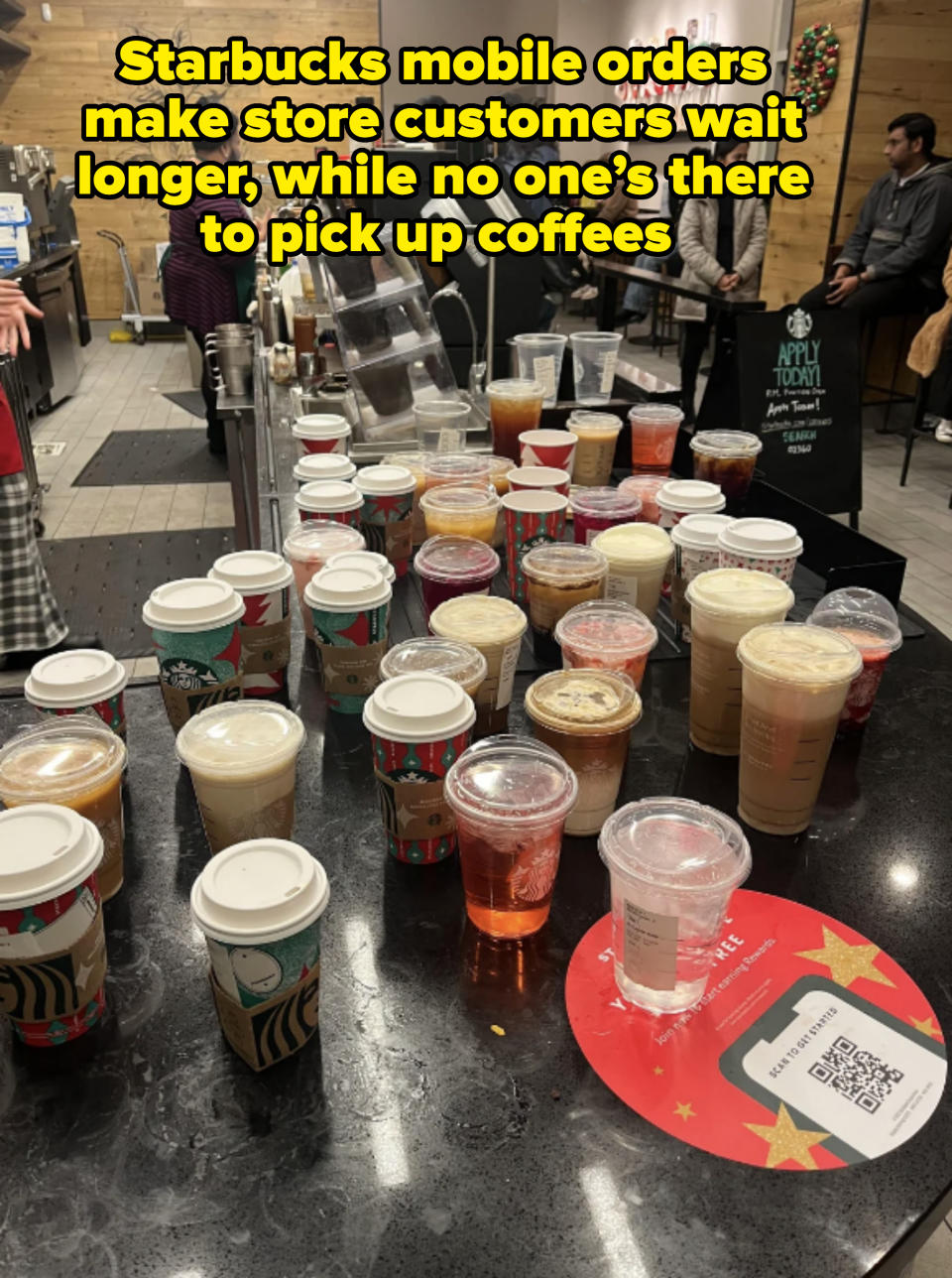 Multiple beverage cups on a counter at a coffee shop, with people waiting in the background