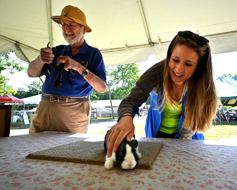 Sterling Greenery employee Elisabeth Wade of Fitchburg stops to pet a bunny at the Cottontail Rabbit Club table while Bob Johnson of Bolton works on the sound system early Saturday morning during the Bolton Fair.