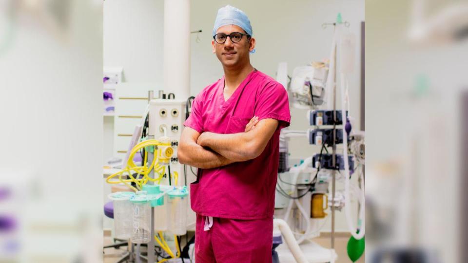 A doctor wearing pink scrubs standing in an operating theatre with his arms folded