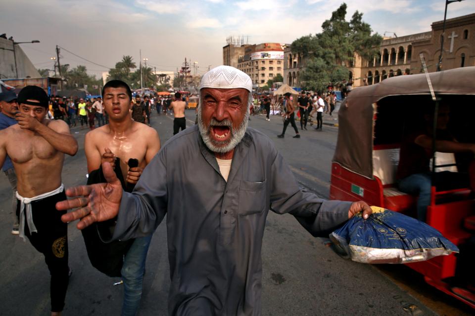 Anti-government protesters run for cover while security forces use tear gas to disperse them on the closed Joumhouriya Bridge that leads to the Green Zone government areas in Baghdad, Iraq, Sunday, Oct. 25, 2020. Thousands of Iraqi protesters have taken to the streets to mark one year since mass anti-government demonstrations swept Baghdad and Iraq's south. Protesters marched Sunday in the capital and several southern cities to renew demands to bring an end to corruption perpetuated by Iraq's politicians. (AP Photo/Khalid Mohammed)