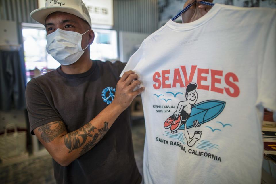 A man displays a white T-shirt with a cartoon surfer carrying a surfboard