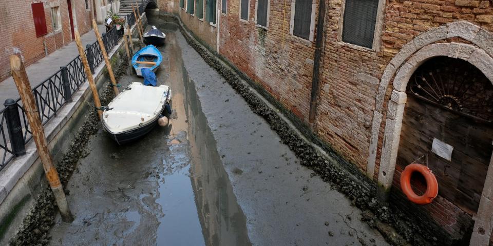 Three Boats are pictured on the dry base of a narrow canal during a severe low tide in the lagoon city of Venice