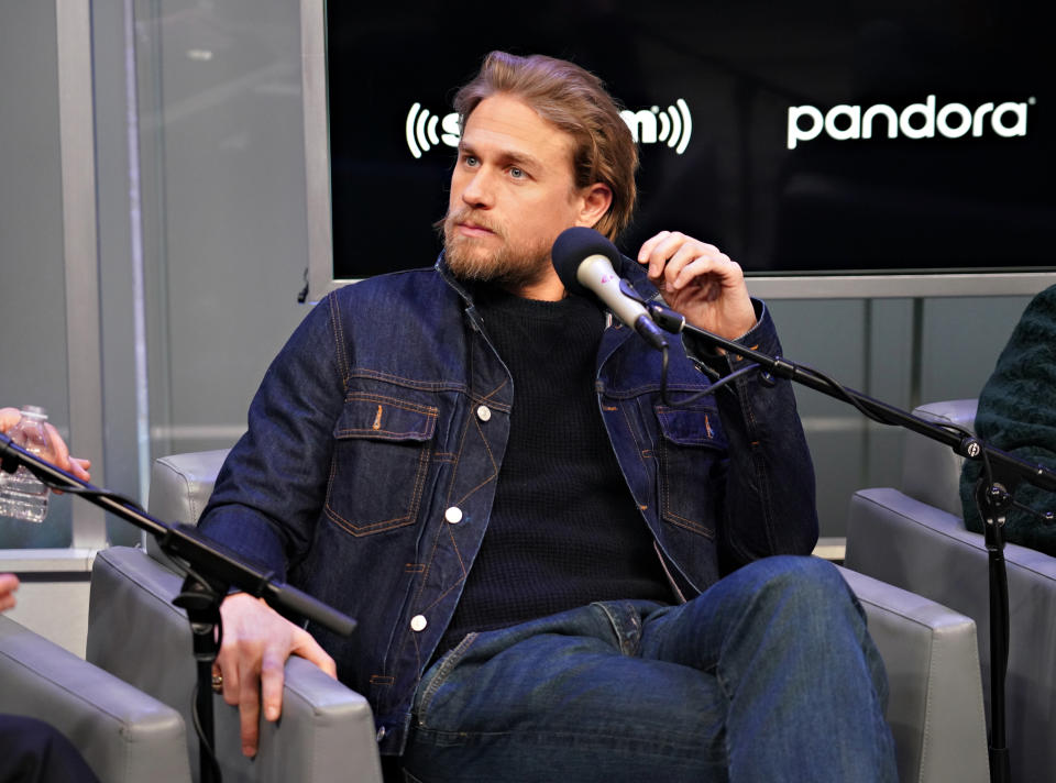 Charlie Hunnam speaks into a microphone during an interview wearing a casual denim jacket and jeans