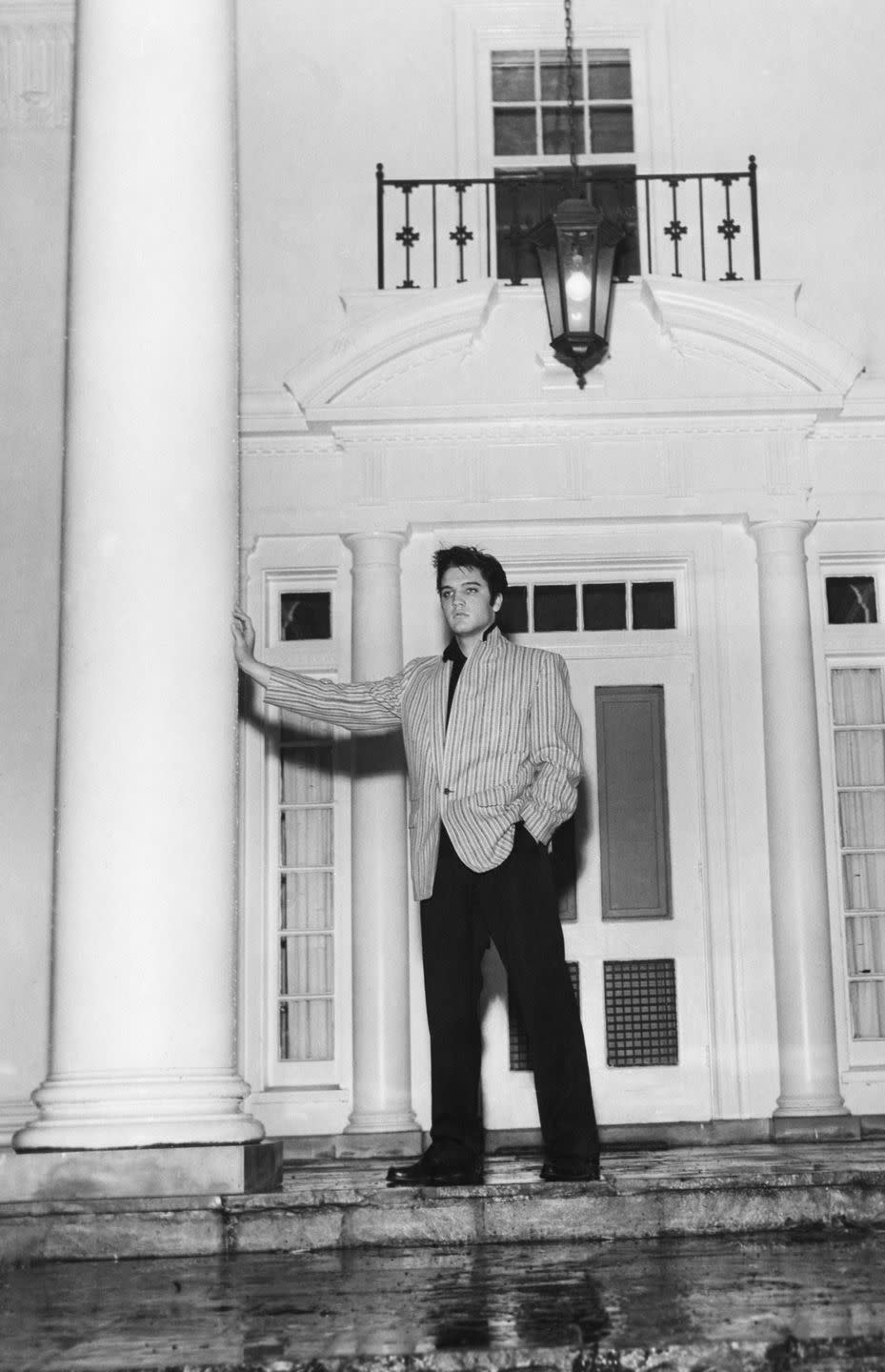 elvis presley leaning against a large column and bracing it with his right arm