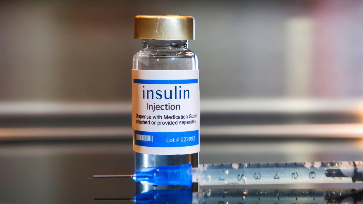 Bottle of insulin injection with a syringe on black table and stainless steel background.