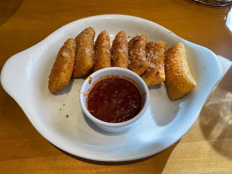 White plate of rectangular shaped mozzarella sticks with a marinara sauce on a brown table at Olive Garden