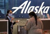 A gate agent with Alaska Airlines assist a traveler at the ticketing counter at Love Field Airport in Dallas, Tuesday, Nov. 24, 2020. (AP Photo/Tony Gutierrez)