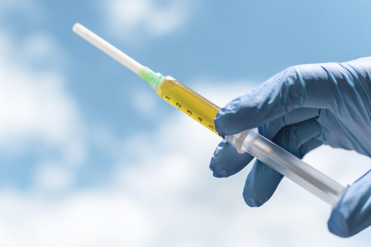 Blood plasma as a hope for treatment of coronavirus infection. Syringe with blood plasma in a hand in a blue medical glove against the sky. Platelet-Rich plasma preparation. Banner, copy space