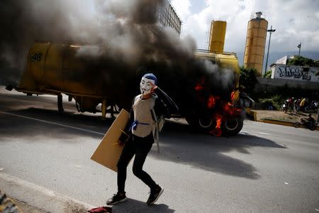 A demonstrator wears a Guy Fawkes mask next to a truck set on fire on a highway during a rally against Venezuela's President Nicolas Maduro's Government in Caracas, Venezuela, June 23, 2017. REUTERS/Ivan Alvarado