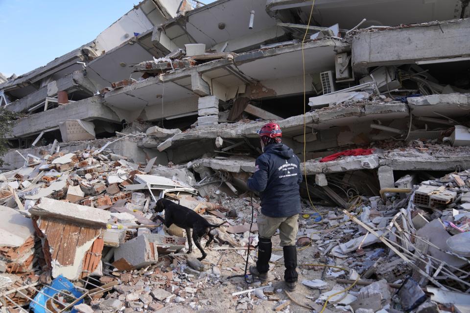 A rescuer with a sniffer dog searches in a destroyed building in Antakya, southeastern Turkey, Friday, Feb. 10, 2023. Rescuers pulled several earthquake survivors from the shattered remnants of buildings Friday, including some who lasted more than 100 hours trapped under crushed concrete after the disaster slammed Turkey and Syria. (AP Photo/Hussein Malla)