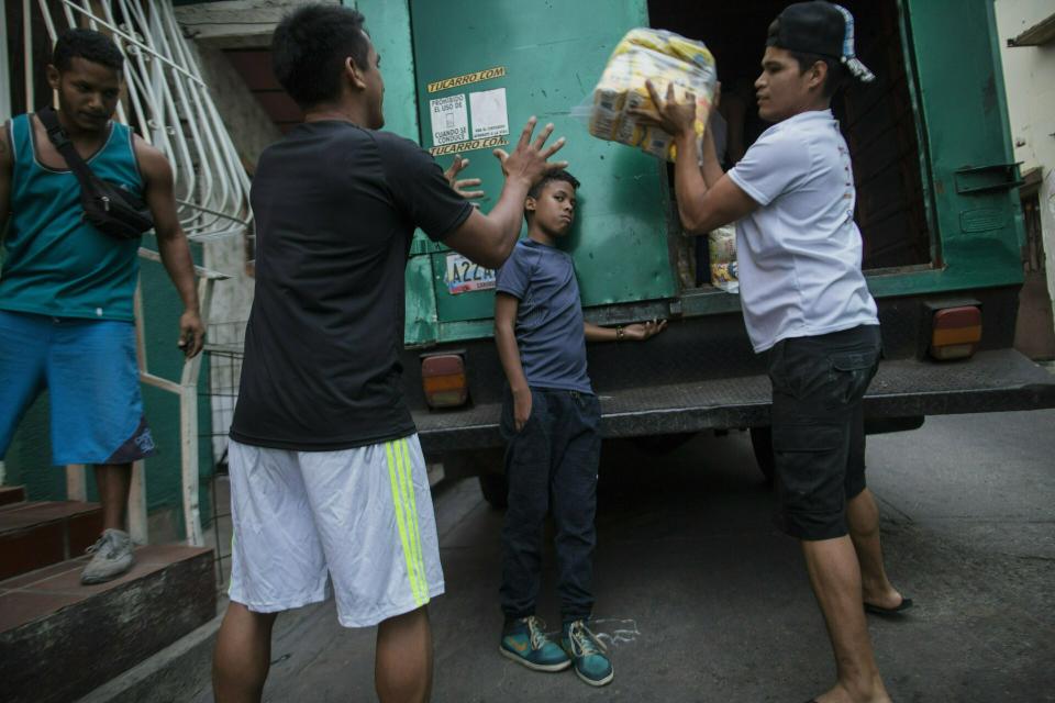 In this Jan. 31, 2019 photo, neighbors unload subsidized food distributed under a government program called "CLAP," in the Catia district of Caracas, Venezuela. The government of Nicolas Maduro has steadfastly denied the existence of a humanitarian crisis that has forced some 3 million Venezuelans to flee the country in recent years, even while relying on the handout of bags of heavily subsidized food staples to rally support among poor. (AP Photo/Rodrigo Abd)