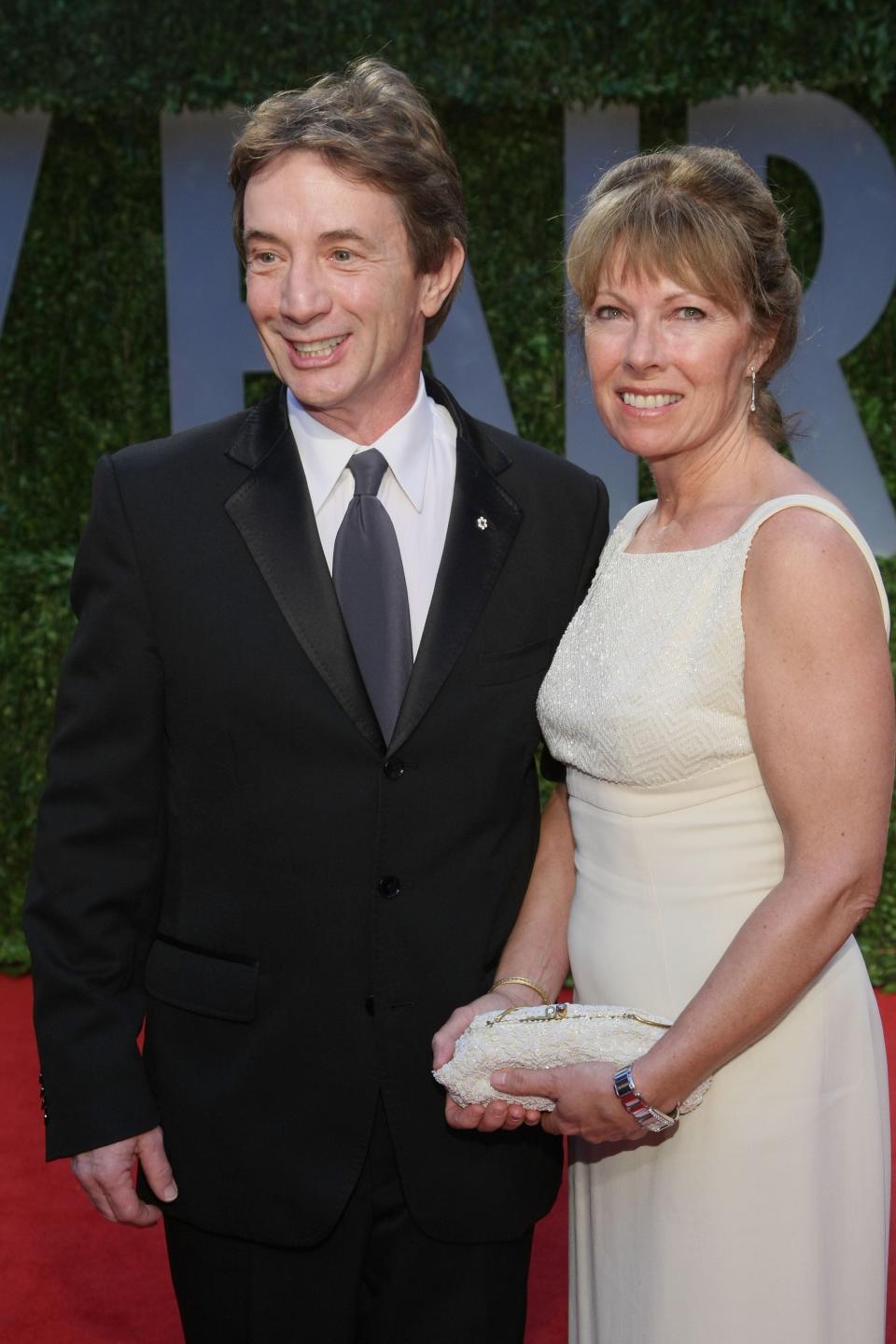 Martin Short, in a black suit and gray tie, posing with wife Nancy Dolman in a white dress on the red carpet