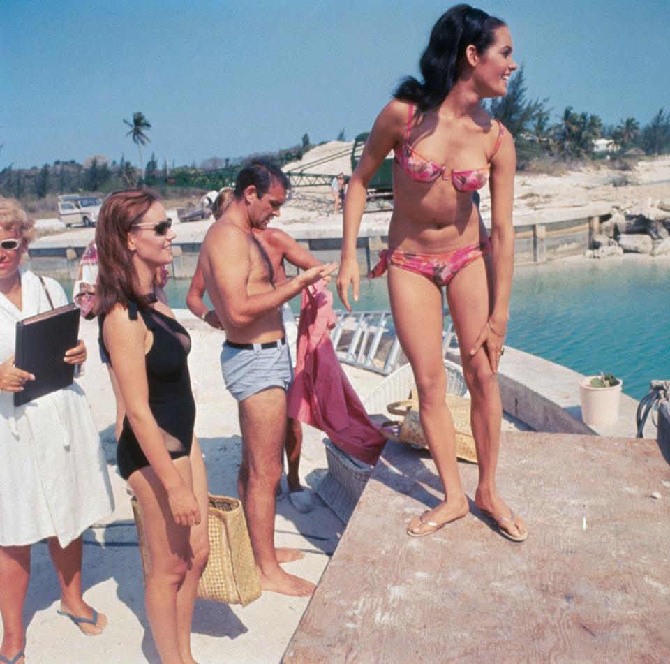 <p>Martine Beswick (pink bikini), Sean Connery (blue trunks) and Claudine Auger (black suit) on set of <em>Thunderball.</em></p>