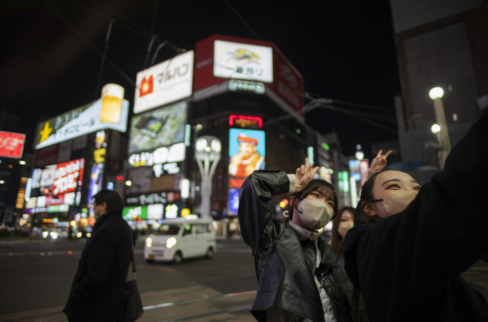 Women try to take a selfie shot at a famed traffic intersection in the Susukino district of Sapporo, northern Japan, Friday, April 14, 2023. G-7 energy and environment ministers are meeting Saturday in the city on the northern Japanese island of Hokkaido ahead of a summit next month. (AP Photo/Hiro Komae)