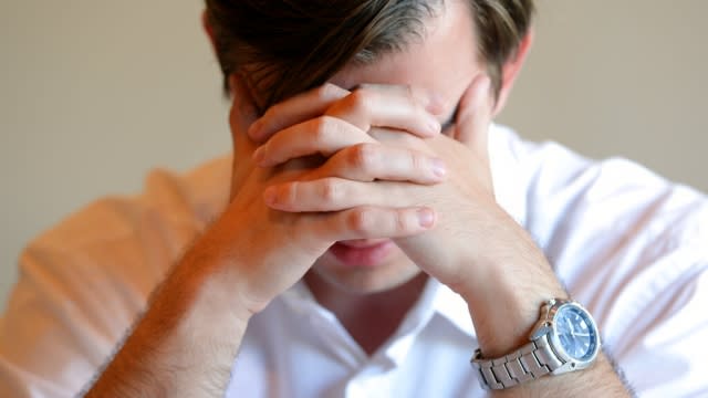 A man looks stressed sits with his hands covering his face