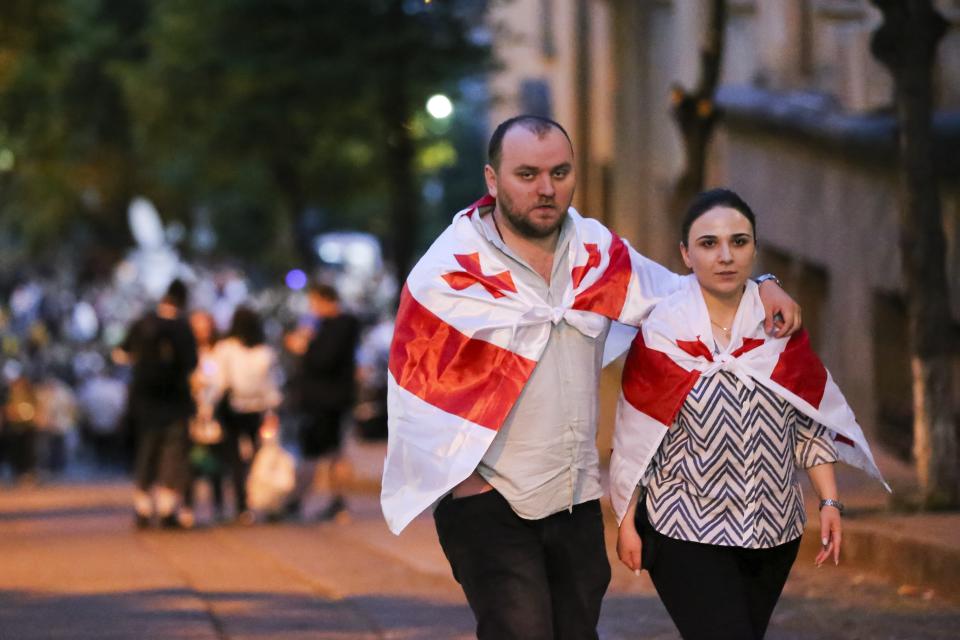 A couple with draped Georgian national flags walk during a protest against "the Russian law" in Tbilisi, Georgia, on Tuesday, April 30, 2024. Clashes erupted between police and opposition demonstrators protesting a new bill intended to track foreign influence that the opposition denounced as Russia-inspired. (AP Photo/Zurab Tsertsvadze)