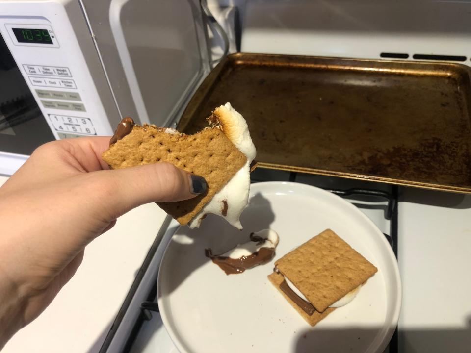 hand holding a smore with a bite taken out of it over a white plate