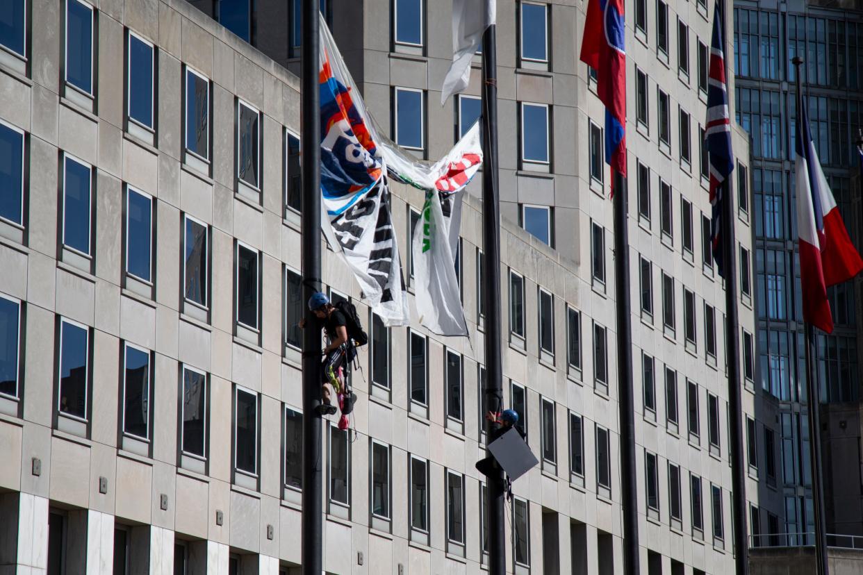 Environmental demonstrators climb flag poles to reveal a large sign in protest of deforestation during Procter & Gamble’s 2022 annual shareholder meeting.