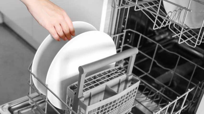 A hand loading dishes into a dishwasher