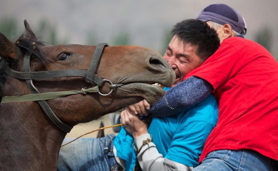 Two men wrestle on horseback.