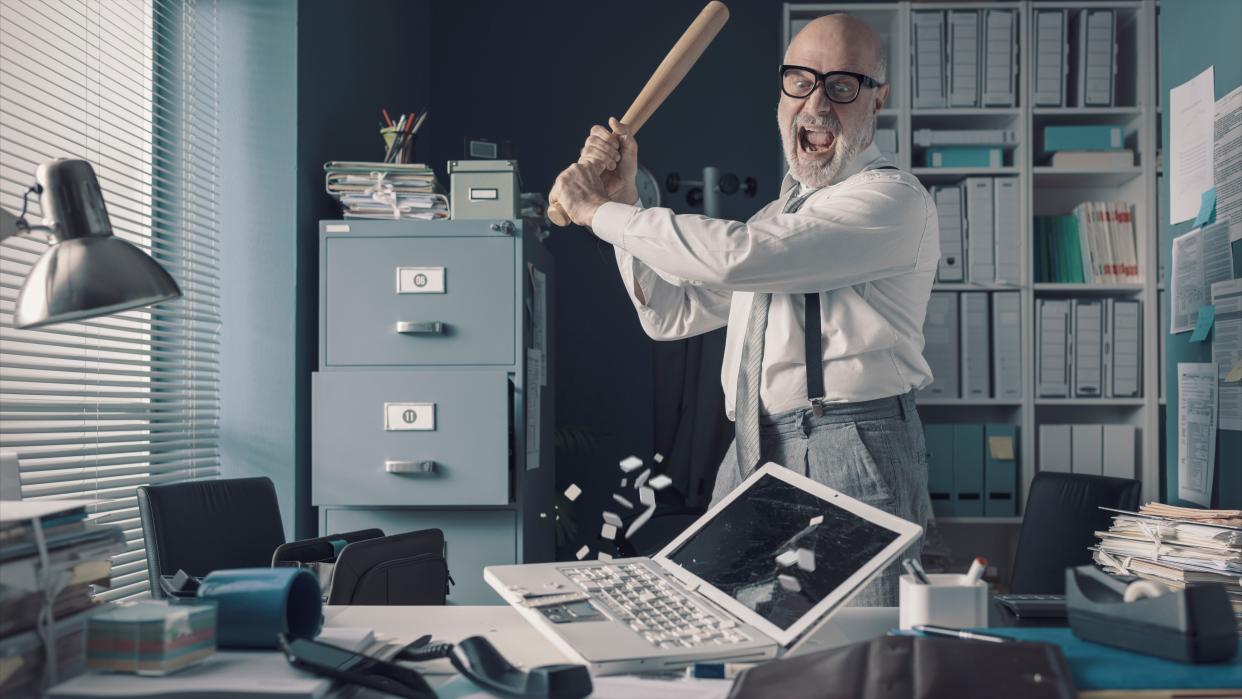  Angry businessman destroying his desk and laptop with a baseball bat 