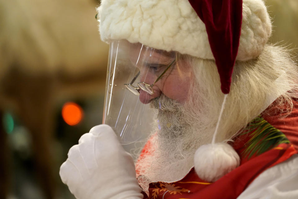 Santa Claus adjusts his protective face shield between visits from children and their families at Bass Pro Shops, in Miami on Nov. 20, 2020. In this socially distant holiday season, Santa Claus is still coming to towns (and shopping malls) across America but with a few 2020 rules in effect. (AP Photo/Lynne Sladky)