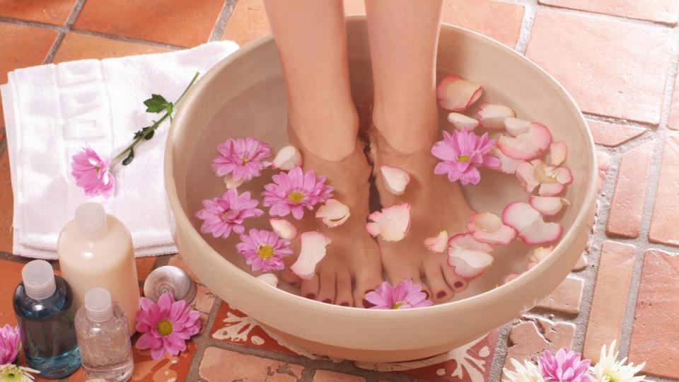 A woman's feet soaking in a bowl filled with flower petals