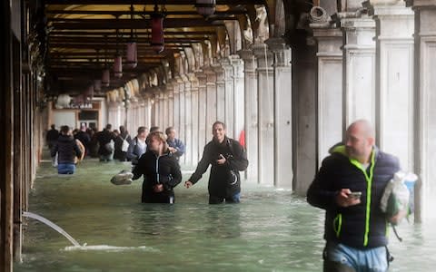 Tourists wade under arches next to the flooded St Mark's Square  - Credit: AFP