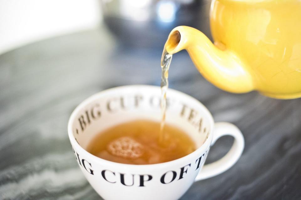 yellow teapot pouring yellow tea into a white teacup