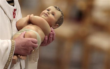 Pope Francis holds the baby Jesus statue at the end of the Christmas night mass in the Saint Peter's Basilica at the Vatican December 24, 2013. REUTERS/Tony Gentile