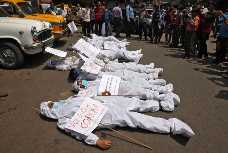 Demonstrators in protective suits and masks lie on a road during a protest demanding to stop election and campaign rallies in the eastern state of West Bengal, in Kolkata