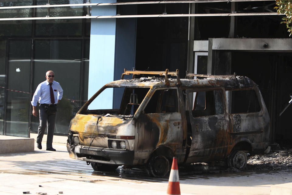 A security guard walks near a destroyed van outside the entrance of Microsoft's offices in northern Athens, Wednesday, June 27, 2012. Assailants attacked the offices of Microsoft early Wednesday, driving a van through the front doors and setting off an incendiary device that burned the building entrance, police said. (AP Photo/Thanassis Stavrakis)