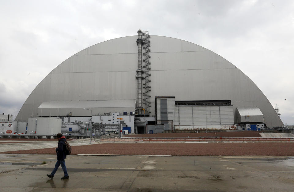 A man walks past a shelter covering the exploded reactor at the Chernobyl nuclear plant, in Chernobyl, Ukraine, Thursday, April 15, 2021. The vast and empty Chernobyl Exclusion Zone around the site of the world’s worst nuclear accident is a baleful monument to human mistakes. Yet 35 years after a power plant reactor exploded, Ukrainians also look to it for inspiration, solace and income. (AP Photo/Efrem Lukatsky)