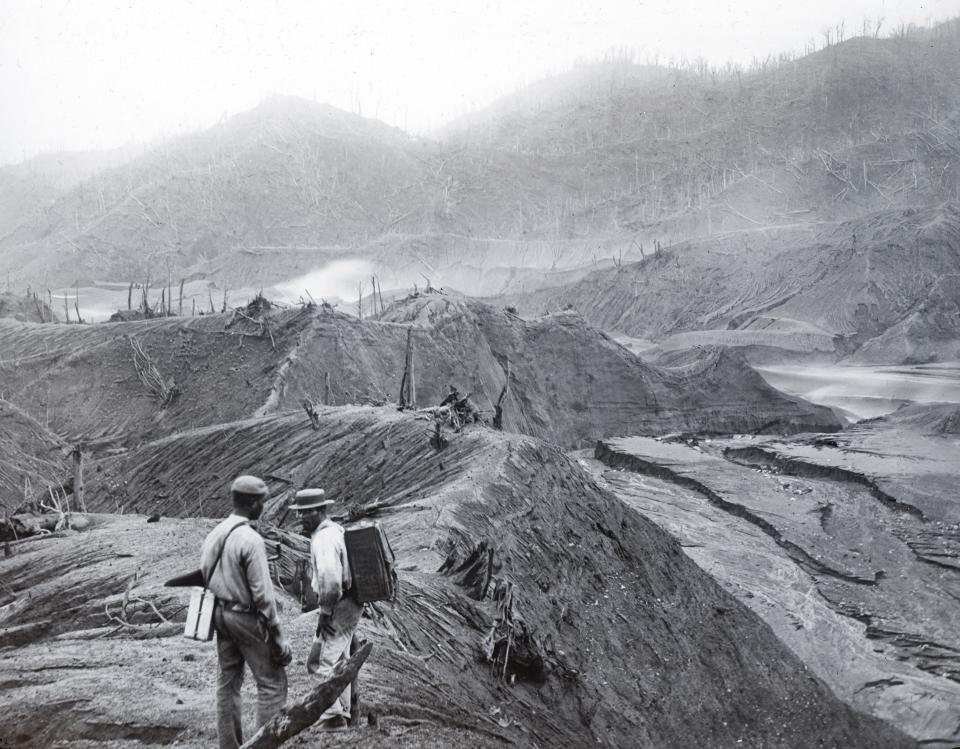 In this 1902 photo provided by York Museums Trust, men survey the devastation of the landscape following eruptions of La Soufrière, a volcano on the island of St. Vincent in the Caribbean. On April 9, 2021, La Soufriere once again started spewing hot torrents of gas, ash and rock, forcing thousands to evacuate to government-run shelters and private homes. (Tempest Anderson/York Museums Trust via AP)