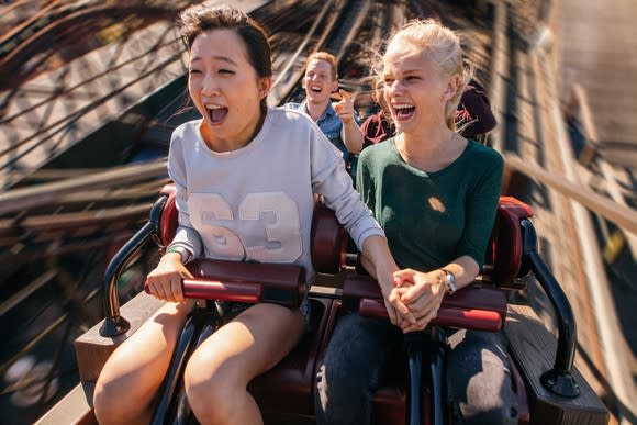 People holding hands while riding on a roller coaster that's going up.