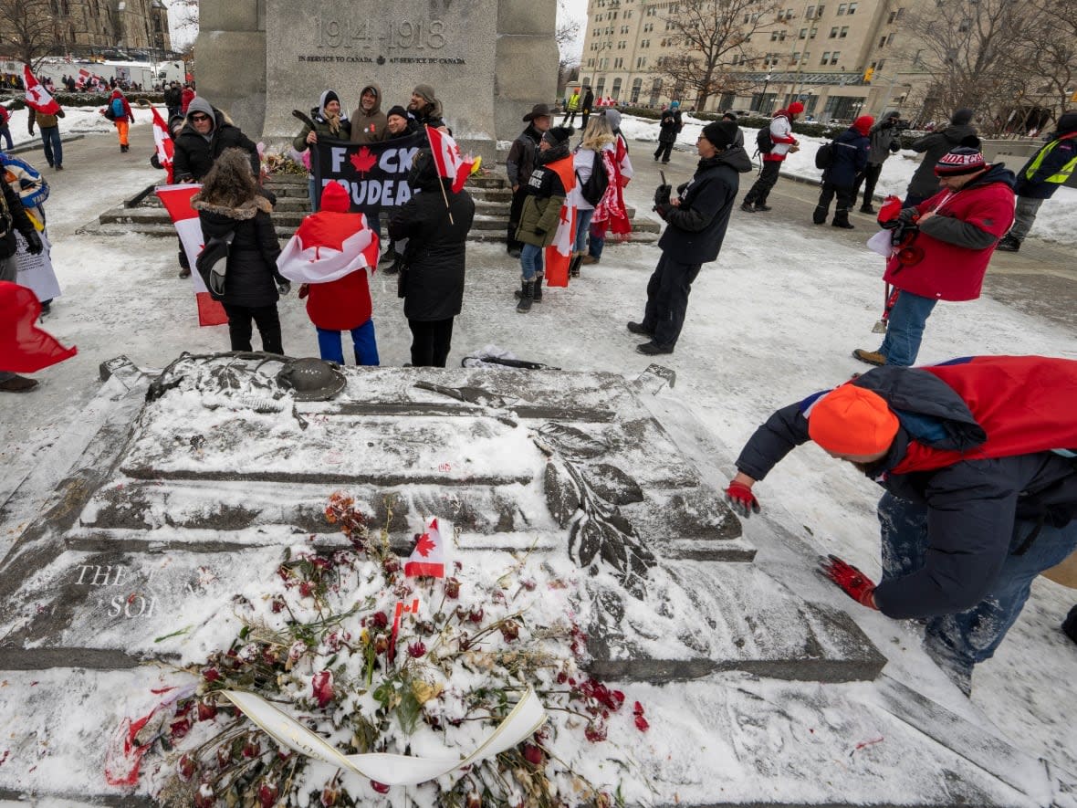 Protesters against COVID-19 restrictions pose for photos with their banners in front of the National War Memorial in Ottawa, as veterans clear snow and ice off the Tomb of the Unknown Soldier on Saturday.  (Frank Gunn/The Canadian Press - image credit)