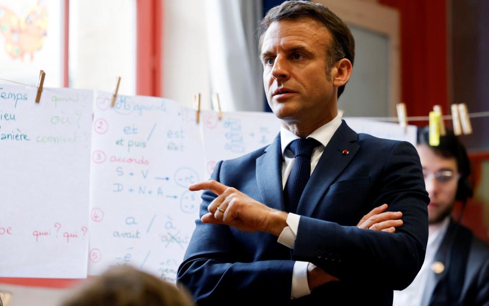 Macron wears a suit and tie and speaks to an unseen class of schoolchildren