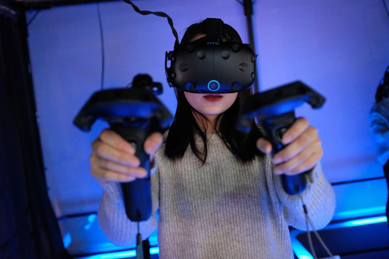 A woman plays a video game using a virtual-reality headset at an arcade.