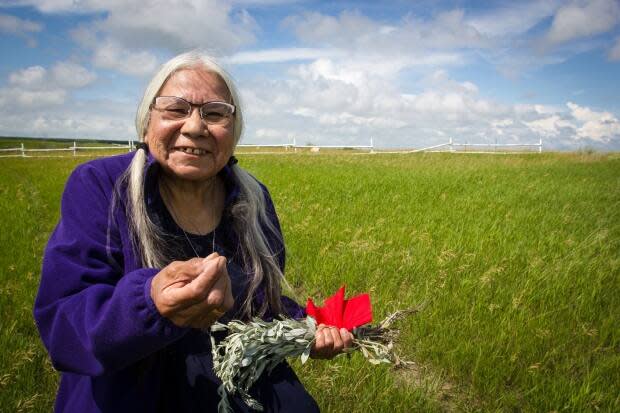 Kokum standing where her family home once stood on Peepeekisis First Nation in southern Saskatchewan, holding sage.