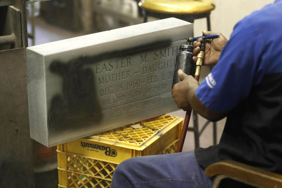 With a stencil only exposing the sandblasted letters, Thursday, May 28, 2020, Leon Brown spray paints the letters black at Elmo's Tombstone Service on Chicago's Southside. (AP Photo/Charles Rex Arbogast)