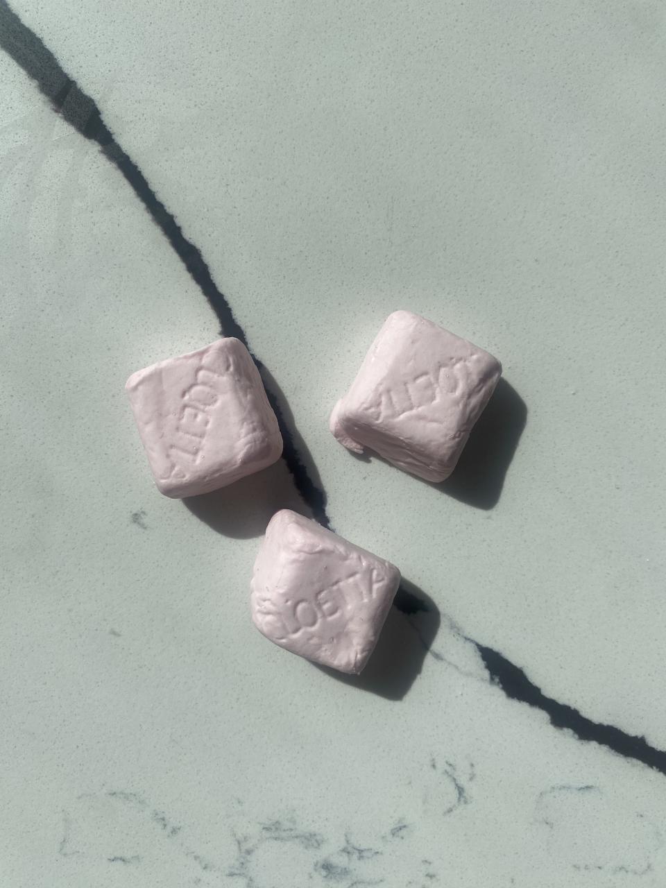 Three light pink, cube-shaped marshmallows; they are arranged on marble surface