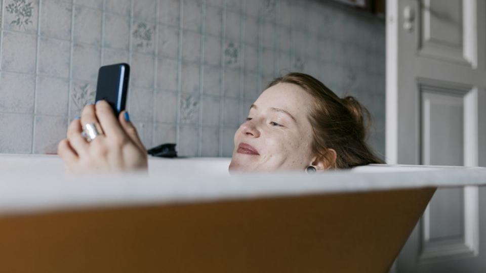 woman taking bath and smiling while messaging someone