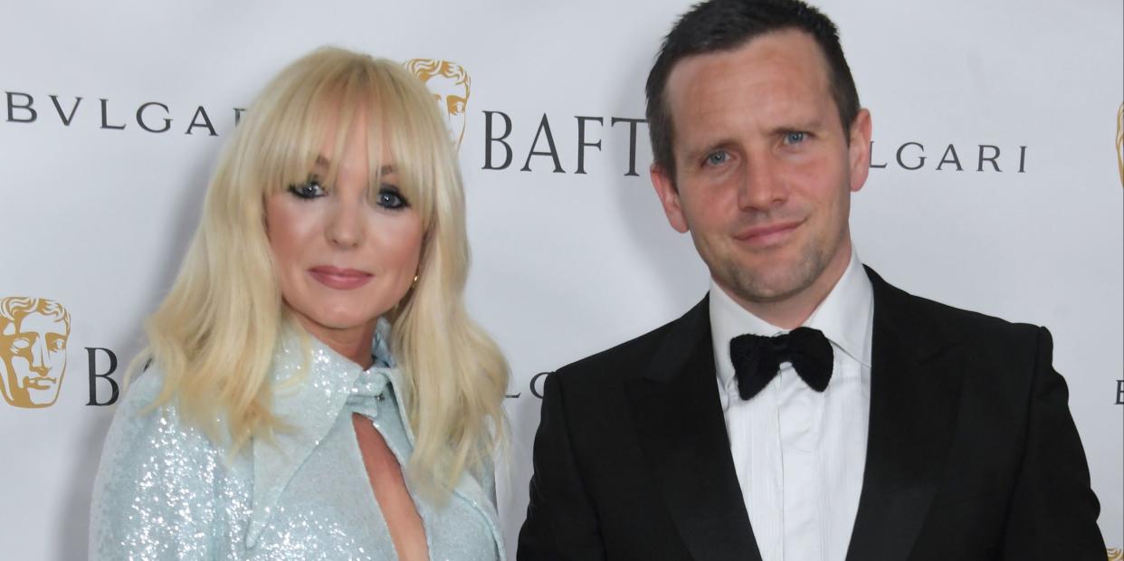 helen george and jack ashton stand holding hands and smiling at the camera, a woman with blond hair down to shoulders and fringe wears a silver sequin dress with feather sleeves, while her husband wears a black suit and bow tie