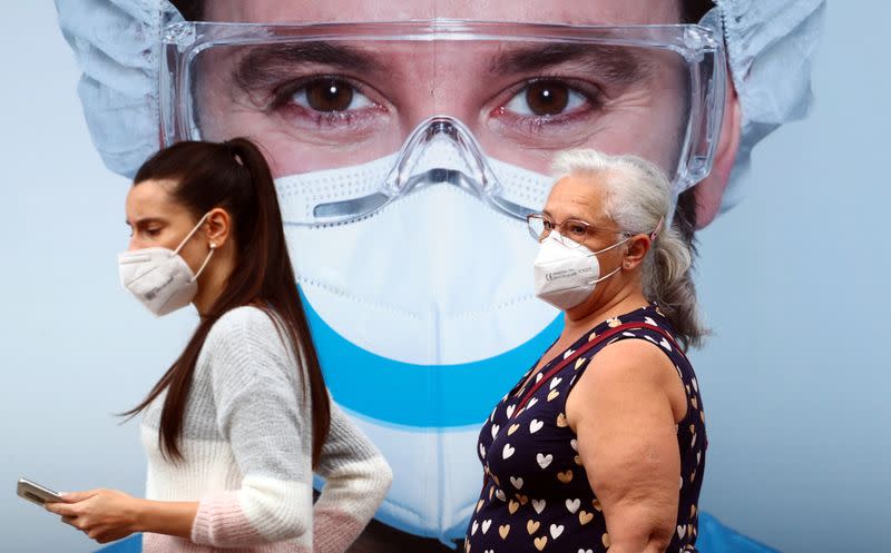 People, wearing protective face masks, walk past a dental clinic advertisement at Vallecas neighbourhood in Madrid