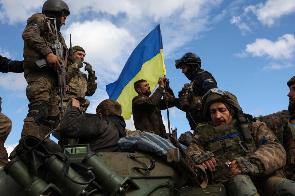 TOPSHOT - Ukrainian soldiers adjust a national flag atop a personnel armoured carrier on a road near Lyman, Donetsk region on October 4, 2022, amid the Russian invasion of Ukraine. - Ukraine's President Volodymyr Zelensky said on October 2, 2022 that Lyman, a key town located in one of four Ukrainian regions annexed by Russia, had been 
